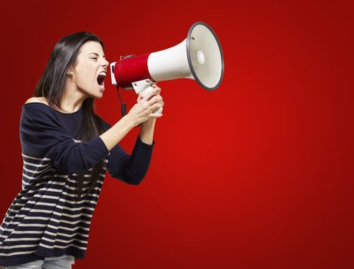 Young woman shouting into megaphone with red background