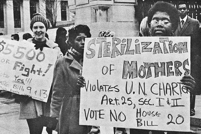 [Black and White Photo: Group of protesters, in foreground a Black woman holds a protest sign saying: Sterilization of Mothers violates UN Charter Afrticle 25, Vote No House Bill 20]