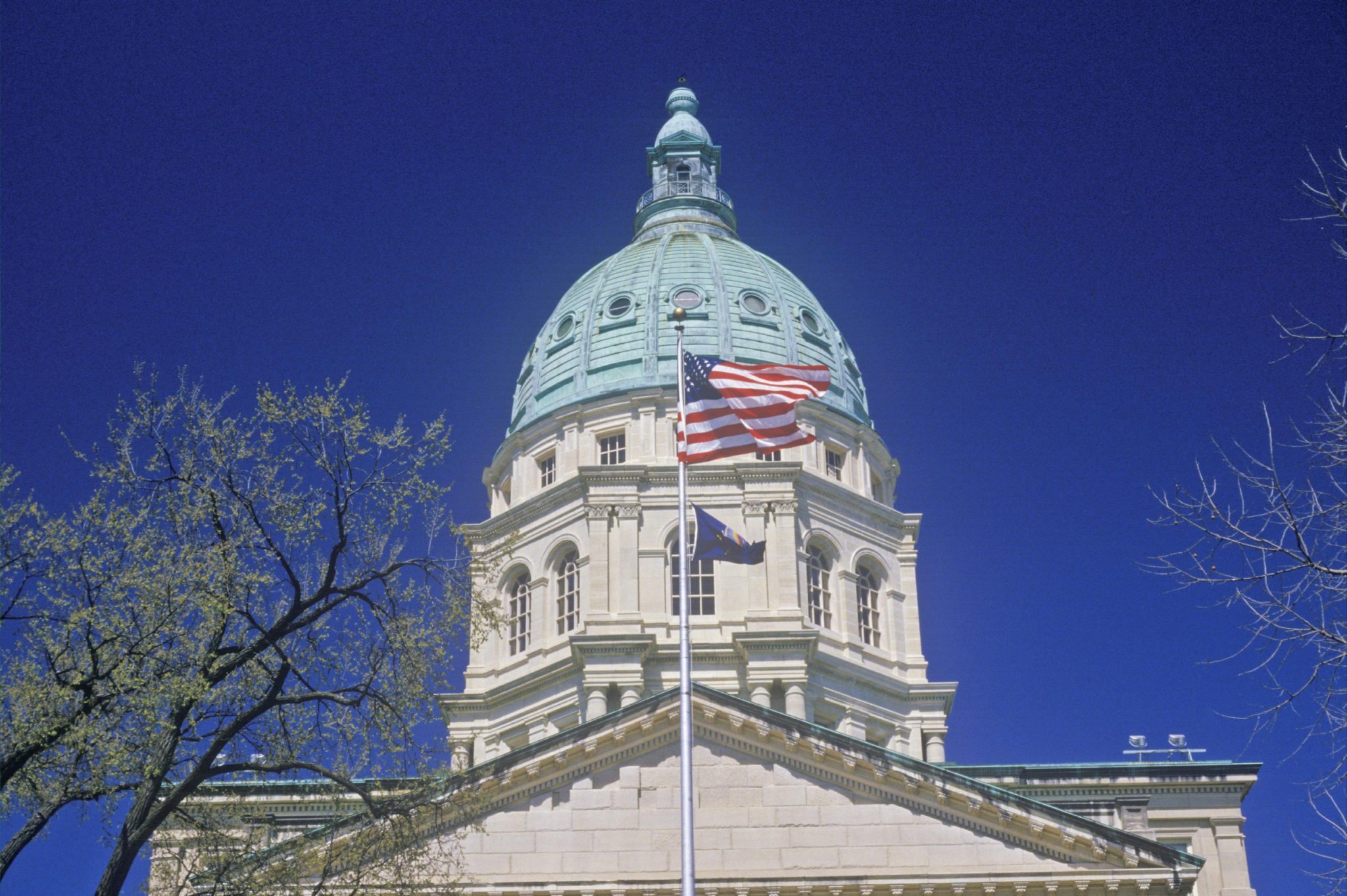Dome of the Kansas state capitol with an American flag flying in front.