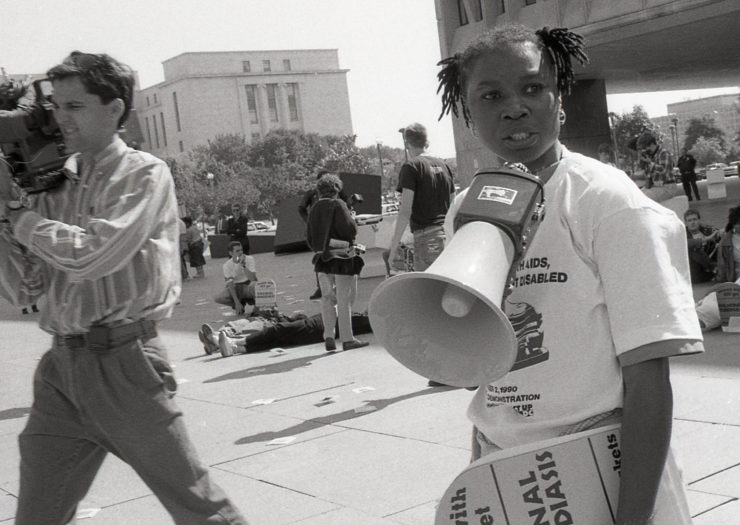 Black and white photo of a demonstration in the late '80s. In the foreground, a black woman stands with a megaphone.
