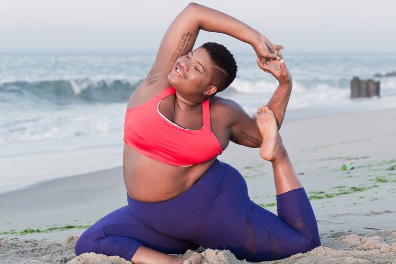 Young Slim Flexible Black Woman Doing Wheel Pose On The Beach