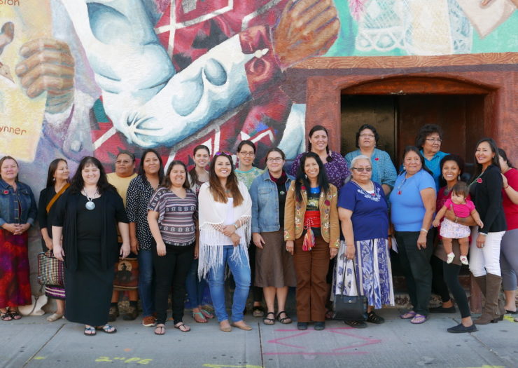 Photo: A group of Native women stand in front of a painted wall.