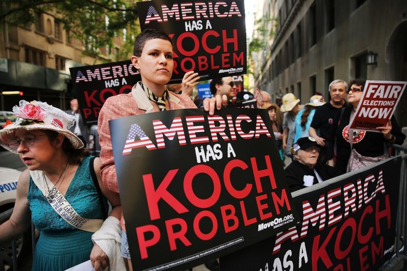 [Photo: Protesters hold up signs that read