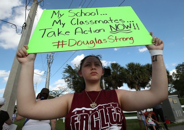 [Photo: A student from Marjory Stoneman Douglas High School holds a sign near the school. The sign reads 