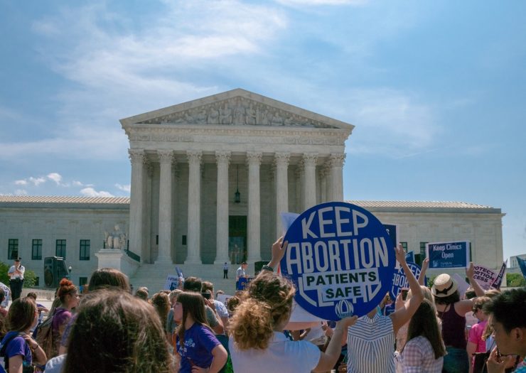 [Photo: A crowd rallies outside of the U.S. Supreme Court. One person holds a sign that reads 