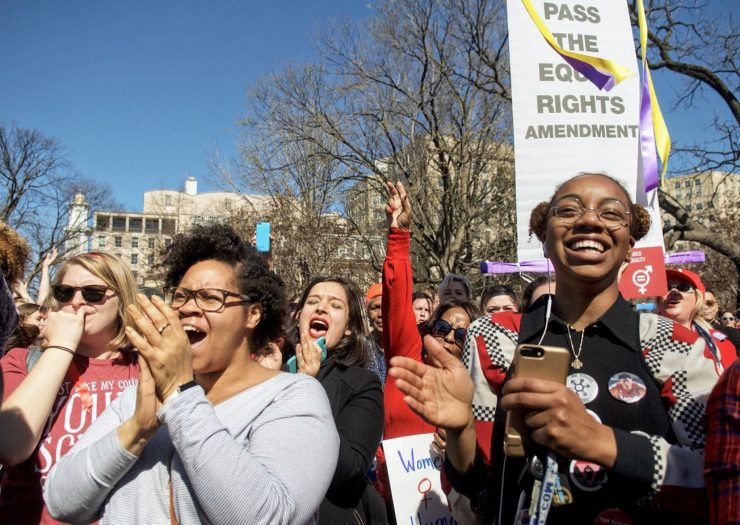 [Photo: Two Black women in a crowd cheer during a rally.]