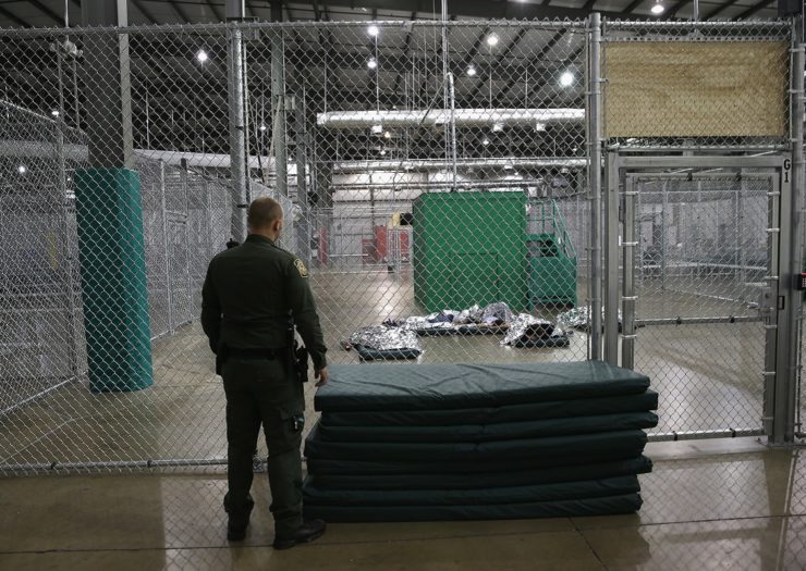 [Photo: A U.S. Border Patrol agent watches as girls from Central America sleep under a thermal blanket at a detention facility run by the Border Patrol.]