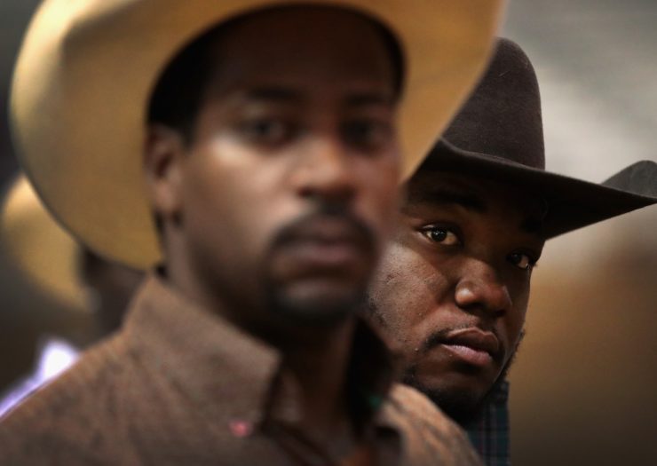 [Photo: Two Black cowboys wearing hats look towards the camera]