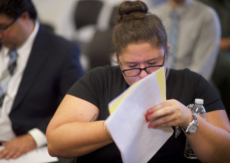 [Photo: A woman holds papers and a water bottle during a job fair.]
