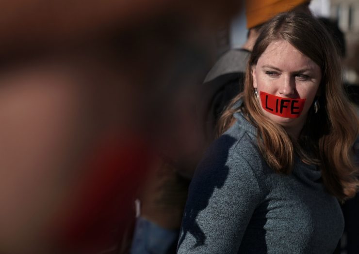 [Photo: A woman with red tape on her mouth with the word 