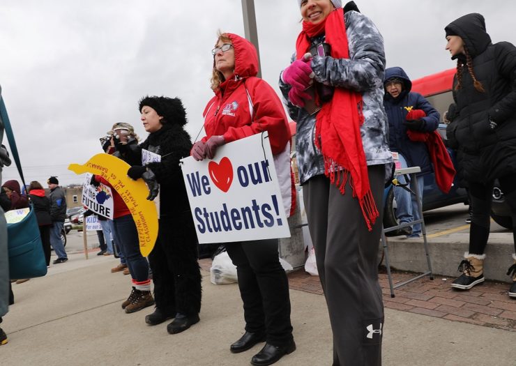 [Photo: West Virginia teachers, students and supporters hold signs on a Morgantown street as they continue their strike.]