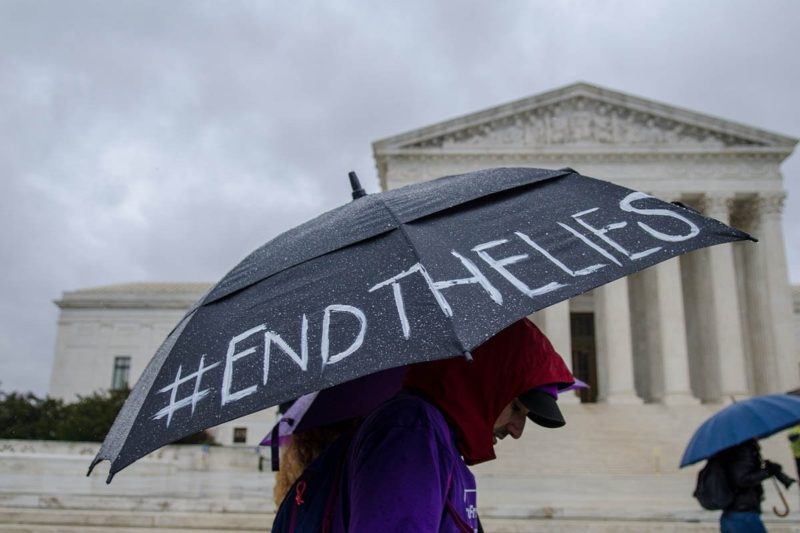 [Photo: An activist carries an umbrella with the hashtag