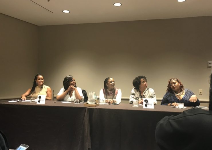 [Photo: Five women sit on a panel during the Power Rising Summit.]
