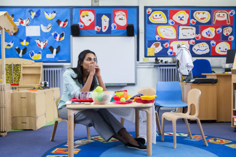 [Photo: A stressed school teacher sits in her elementary school classroom.]