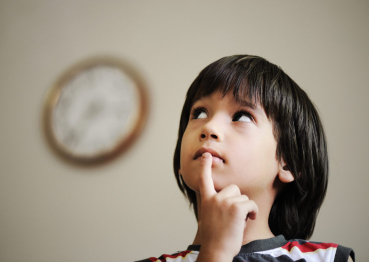 [Photo: A child looking up and thinking next to a clock.]