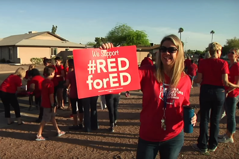 [Photo: A teacher holds a sign that read