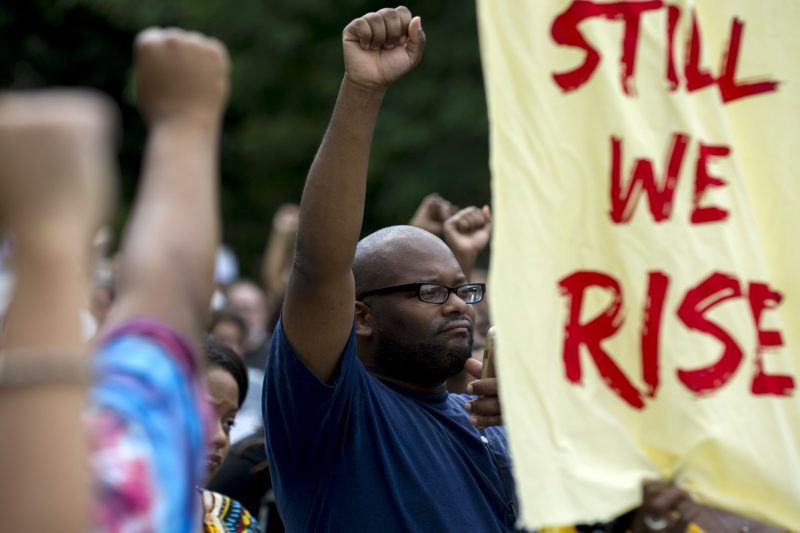 [Photo: A group of Black people gather near a sign that reads
