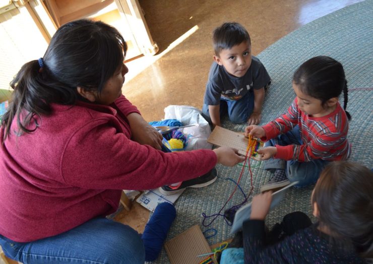 [Photo: A teacher at a Navajo educational facility in Leupp, Arizona, teaches young children in her tribe's language the traditional native weaving techniques.]
