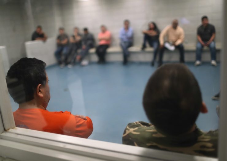 [Photo: Undocumented immigrants wait in an Immigration and Customs Enforcement (ICE), processing center after they were arrested]