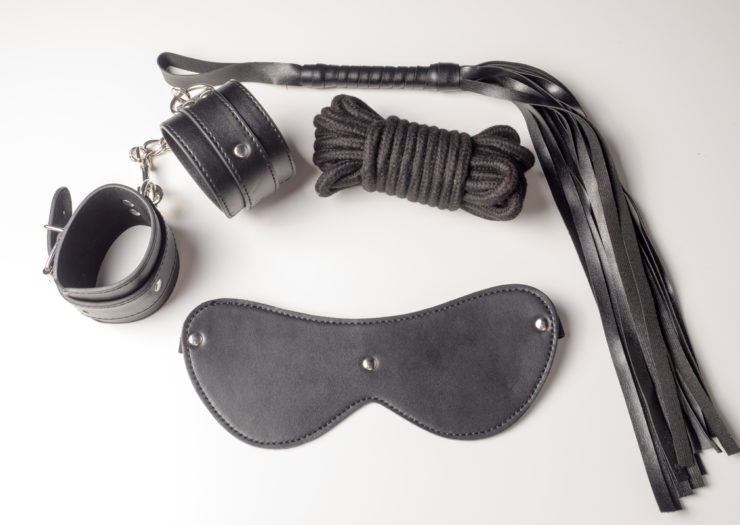 [Photo: Leather handcuffs, leather whip,leather mask and black cord on white background]
