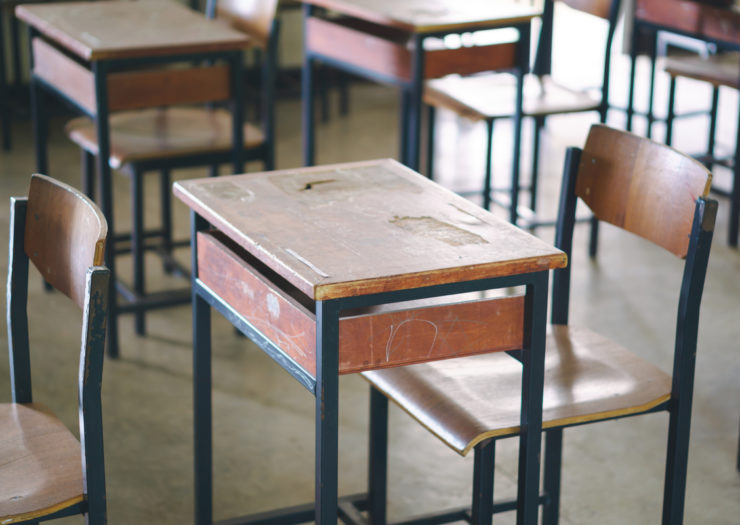 [Photo: An empty classroom with old, dusty tables and chairs]