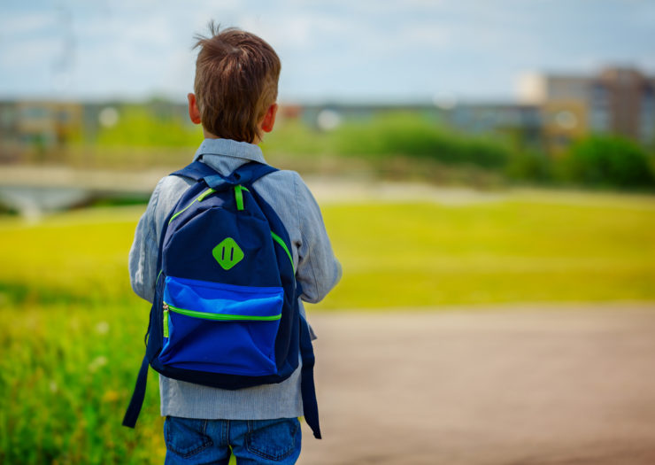 [Photo: A boy with a backpack walks towards school]