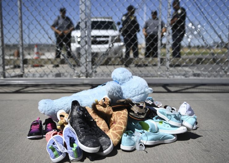[Photo: Shoes and toys sit on the ground next to border patrol agents]
