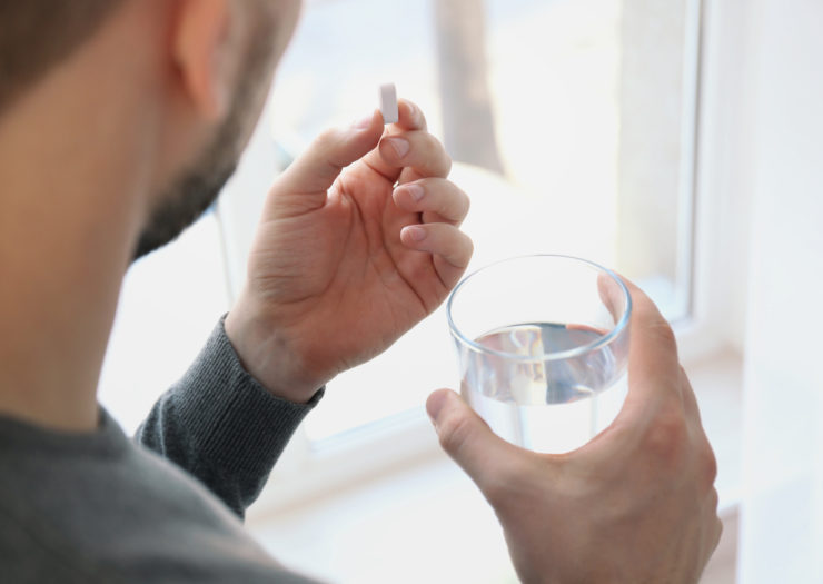 [Photo: A man takes medicine and holds a glass of water]