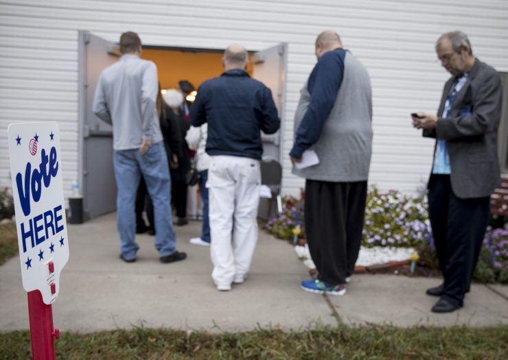 [Photo: people gather outside of a polling place to vote]