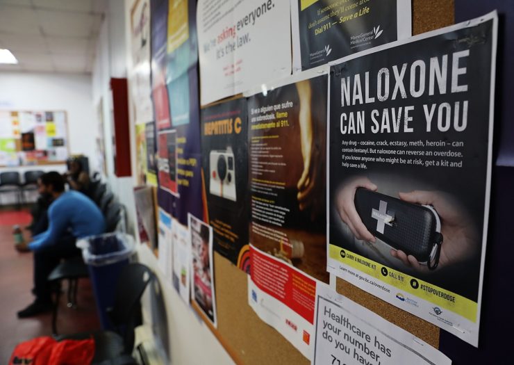 [Photo: A sign for Naloxone hangs on a wall filled with posters in a classroom]