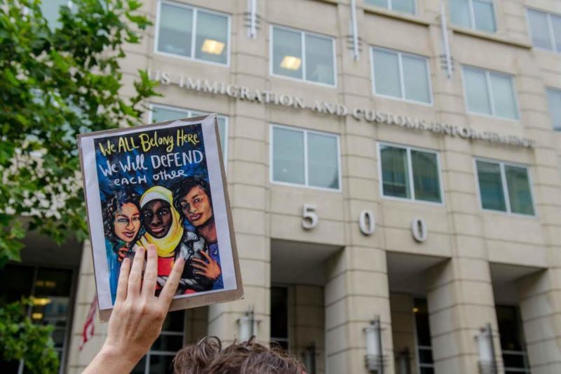 [Photo: A protester holding a sign outside of ICE headquarters that reads,