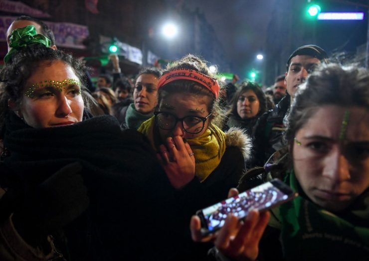 [Photo: Three young woman pro-choice activists hear green and orange headbands that show their support for reform of Argentina's restrictive abortion law.]