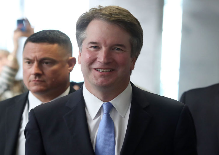 [Photo: Suited white male Supreme Court nominee Brett Kavanaugh smiling and walking.]