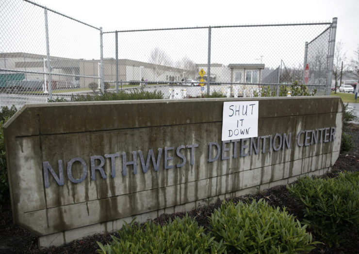 [Photo: Exterior shot of the Northwest Detention Center sign, on which someone posted a paper that reads, 