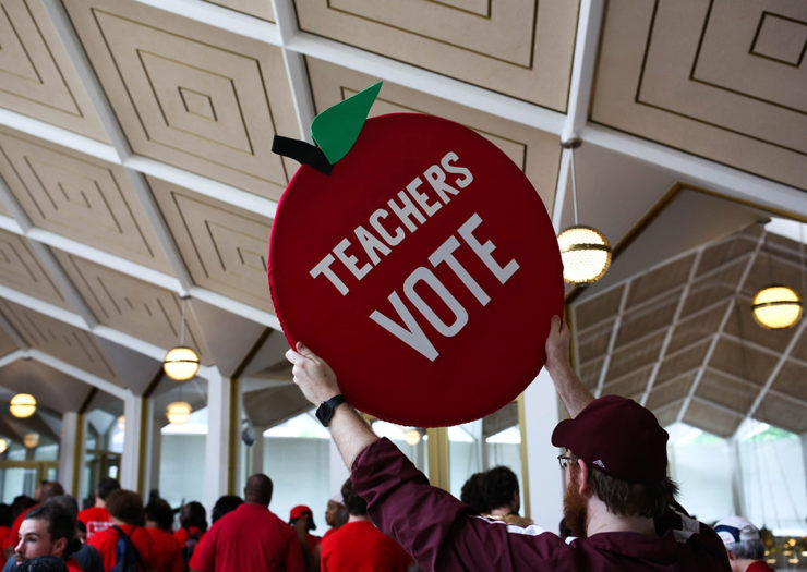 [photo: a protester holds a sign that reads teachers vote.]