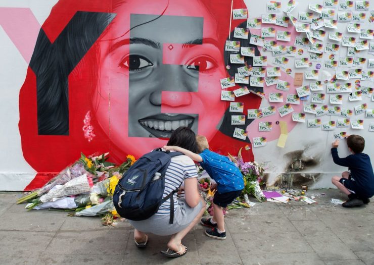 [PHOTO: Red mural of smiling South Asian woman and a woman with small children kneeling.]