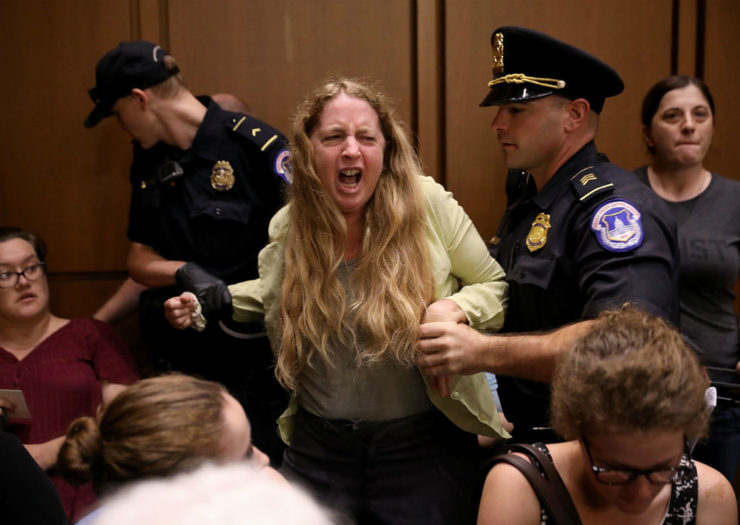 [Photo: Woman being pulled away by police in court hearing.]