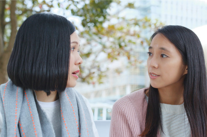 [PHOTO: Two women of Asian descent in conversation outside.]