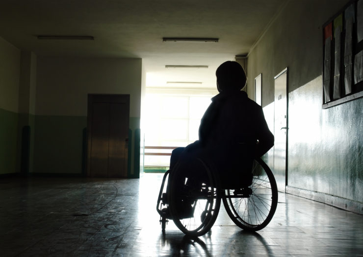 [Photo: A woman in a wheelchair sits in a dark hospital hallway.]