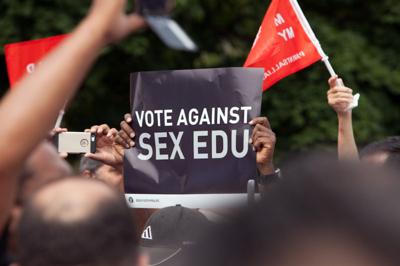 [PHOTO: Hands holding a black and white sign saying