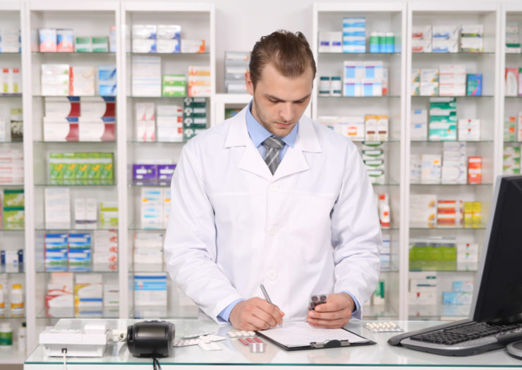[Photo: A male pharmacist stands behind a counter.]