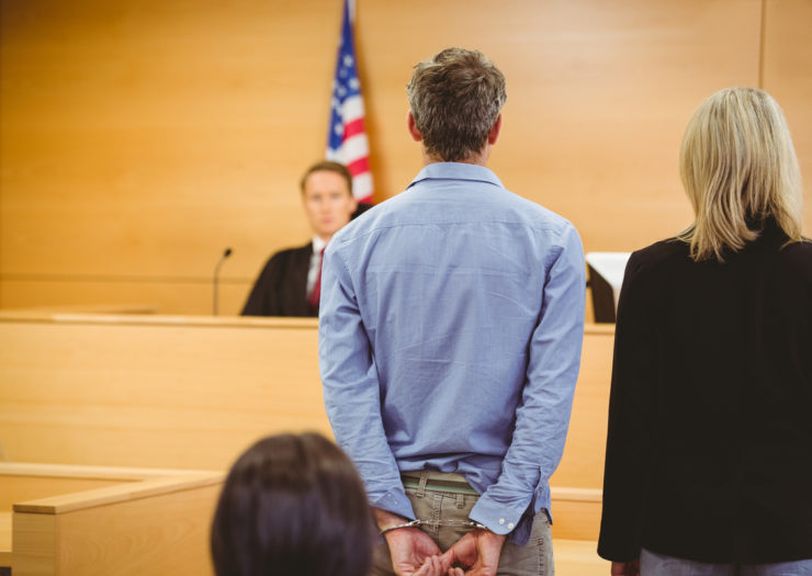 [Photo: A man in handcuffs faces a judge's bench.]