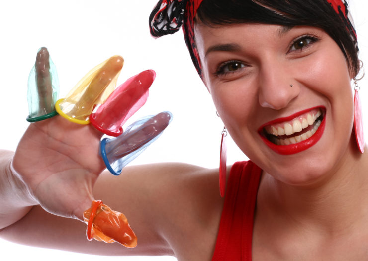 [PHOTO: A smiling woman holds up a hand with a rainbow of male condoms on all five of her fingers.]