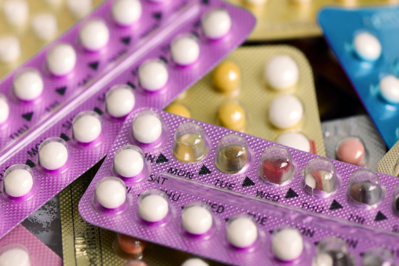 Photo of oral contraceptive pill on pharmacy counter with colorful pills strips background