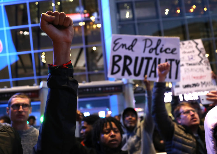 [photo: protesters raise fists against police brutality during a demonstration.]