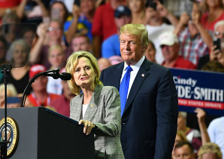 [Photo: Cindy Hyde-Smith speaking at podium with Trump behind her.]