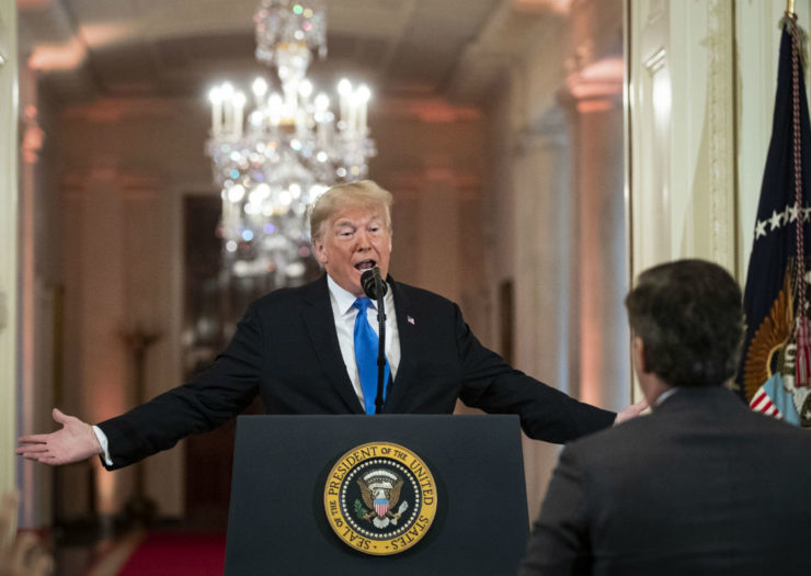 [Photo: Donald Trump with arm outstretched at podium, speaking to a reporter whose back is facing the camera.]