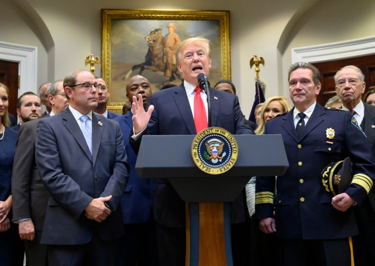 [photo: President Donald Trump speaks at podium flanked by law enforcement officers and politicians to make an announcement on prison reform legislation.]