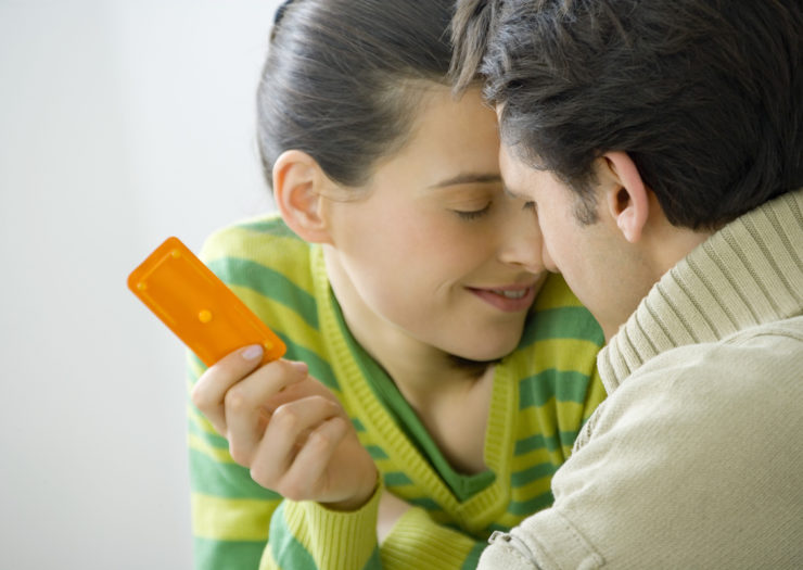 [PHOTO: White woman and men brush noses in a prelude to a kiss. She holds an orange packet that holds one pill.]