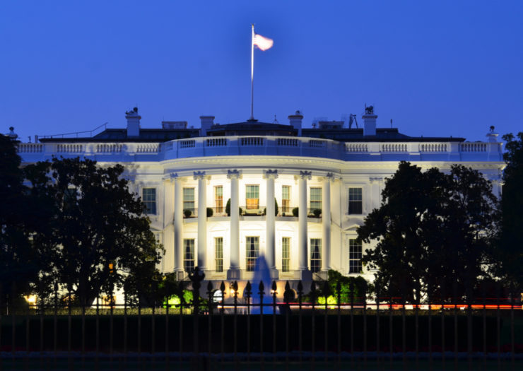 [Photo: The White House in the evening with lights illuminating the front facade.]
